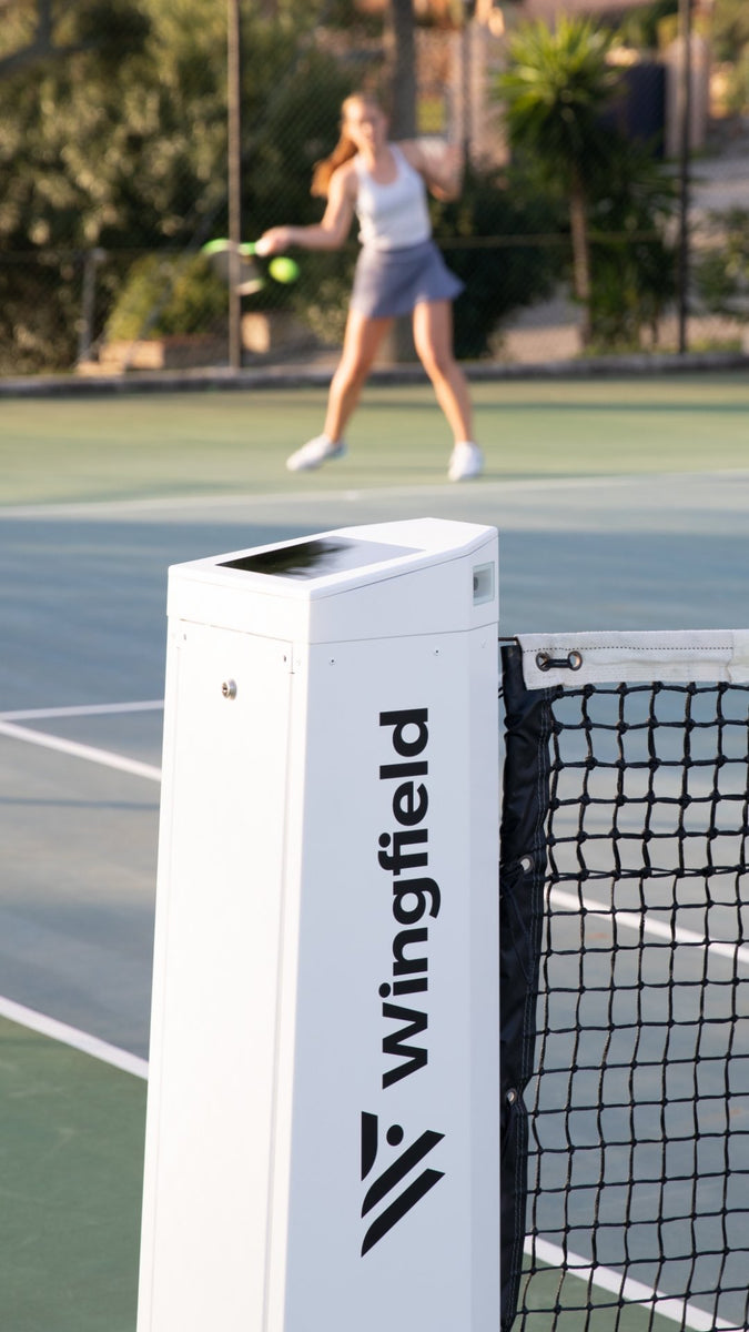 The white Wingfield Box on a hard court. A tennis player in the background.