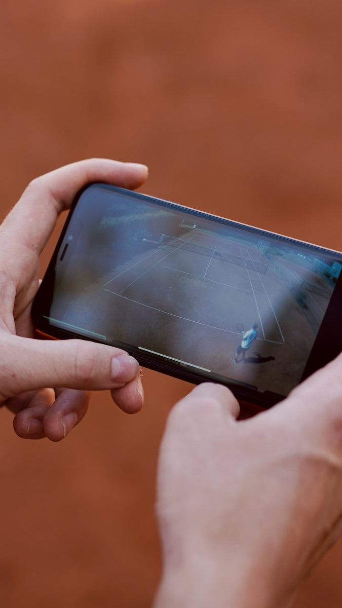 Man holding smartphone with video of tennis match playing.