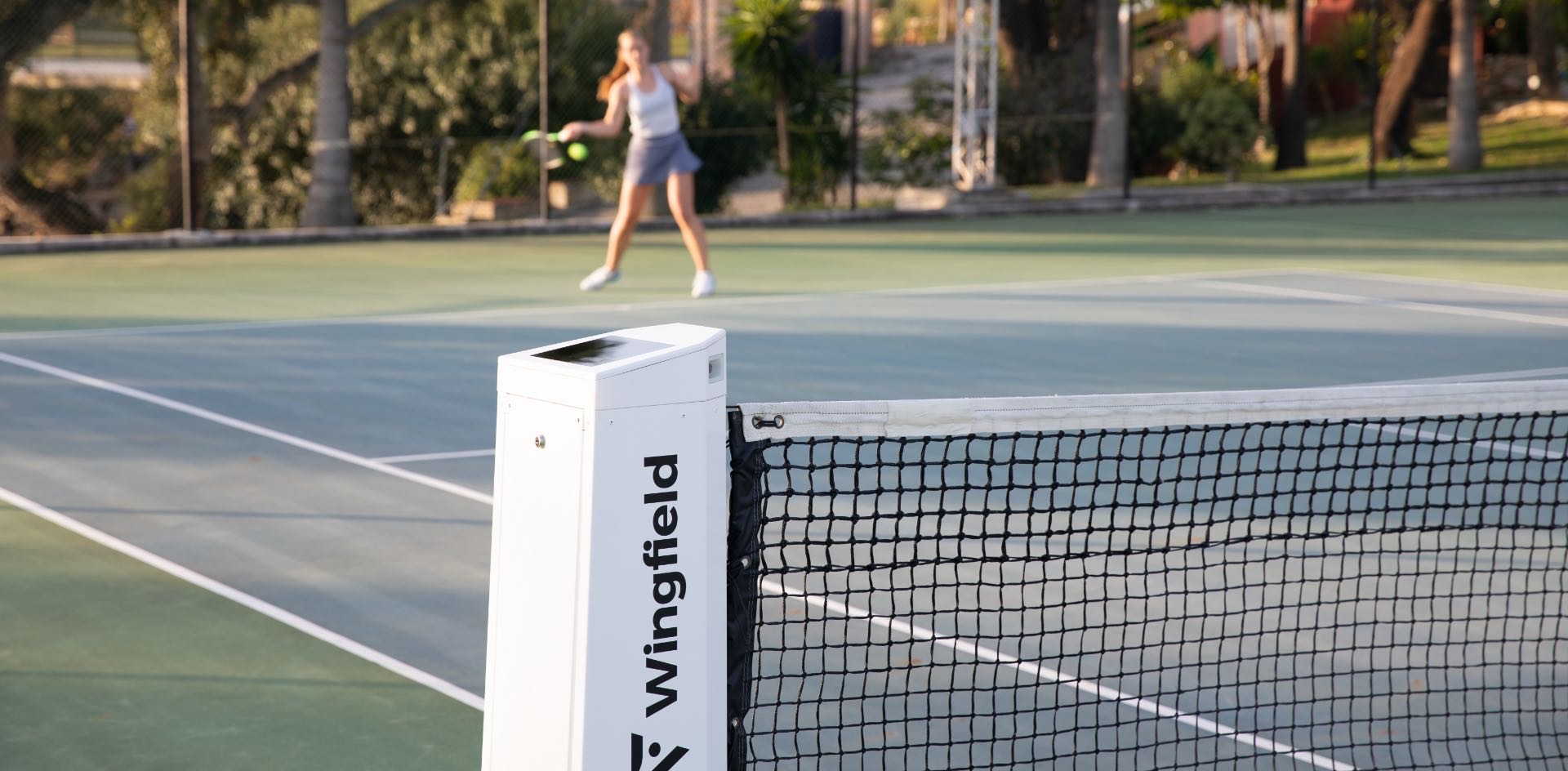 The white Wingfield Box on a hard court. A tennis player in the background.